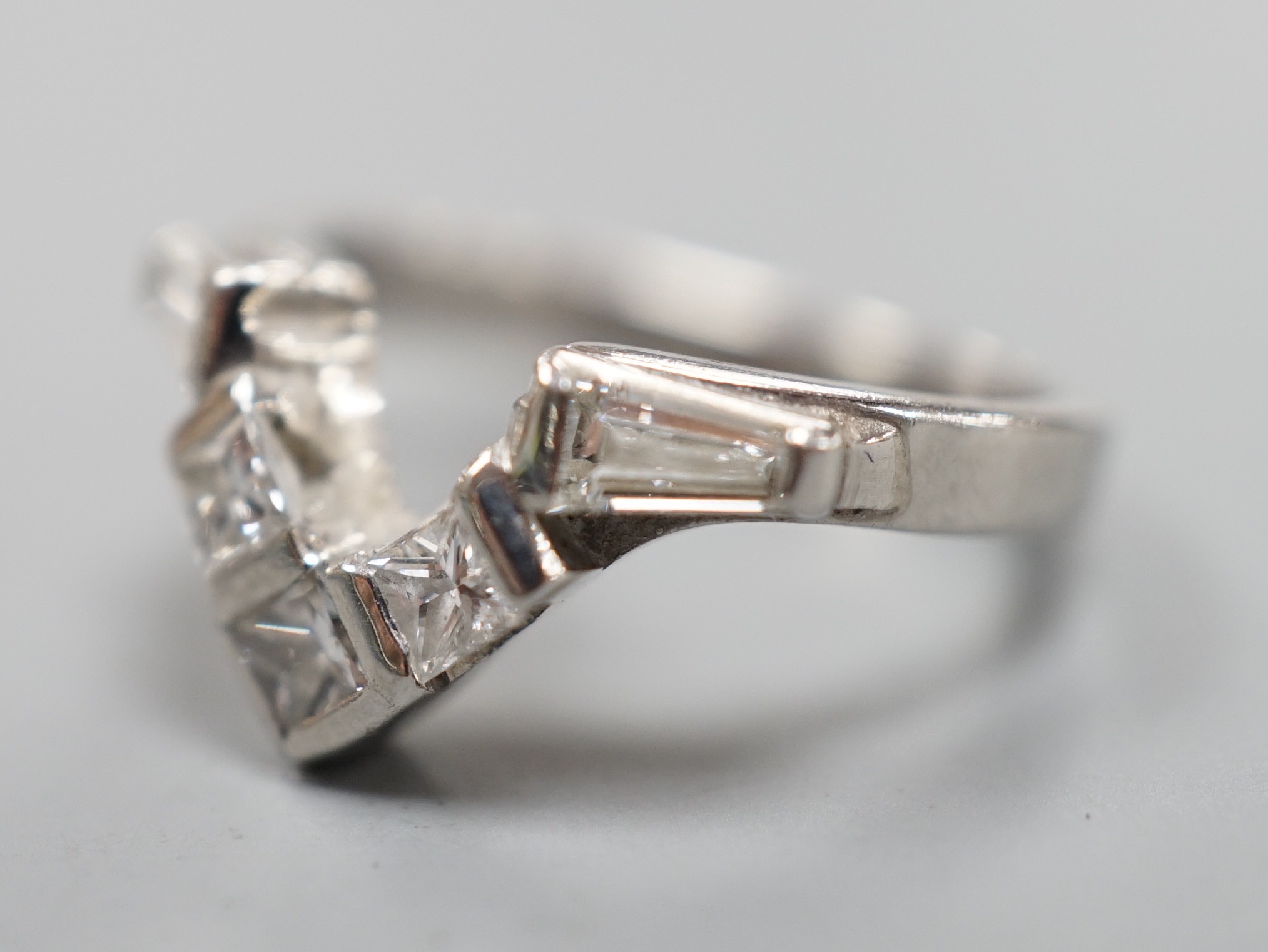 A modern white metal (stamped plat), two stone trapeze cut and three stone princess cut diamond set 'chevron' ring, size I, gross weight 5.3 grams.